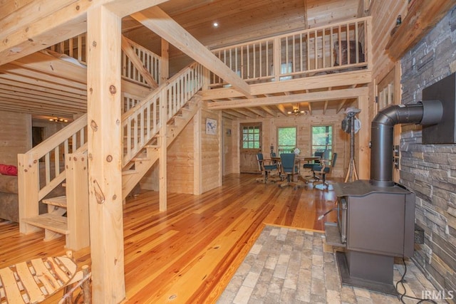 unfurnished living room with wooden walls, a towering ceiling, hardwood / wood-style floors, a wood stove, and stairs