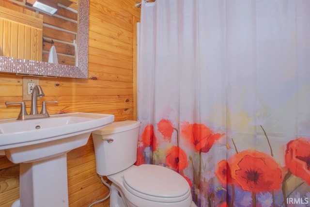 full bath with a shower with curtain, a sink, toilet, and wooden walls