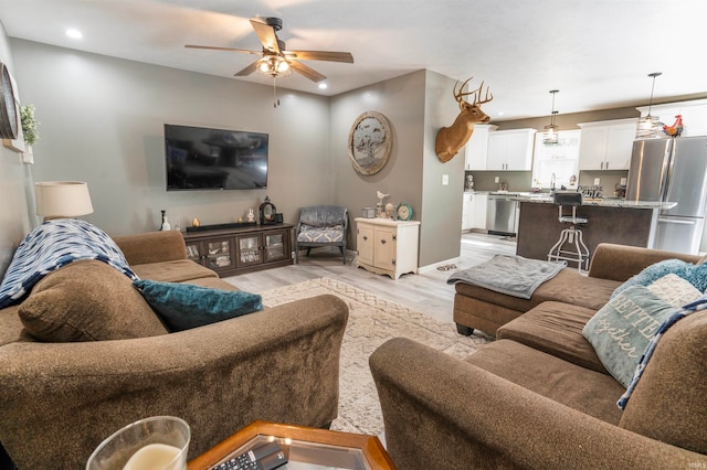 living room featuring light wood-type flooring, sink, and ceiling fan