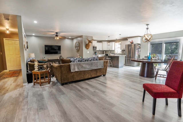 living room with light wood-type flooring and ceiling fan with notable chandelier