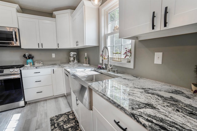 kitchen with light stone countertops, stainless steel appliances, white cabinetry, and light hardwood / wood-style flooring