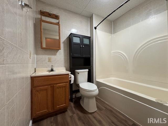 full bathroom with toilet, vanity, wood-type flooring, tile walls, and washtub / shower combination