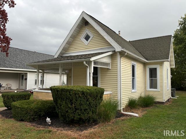 view of home's exterior featuring covered porch, roof with shingles, and a lawn