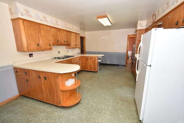 kitchen with white refrigerator, stainless steel gas cooktop, decorative backsplash, and kitchen peninsula