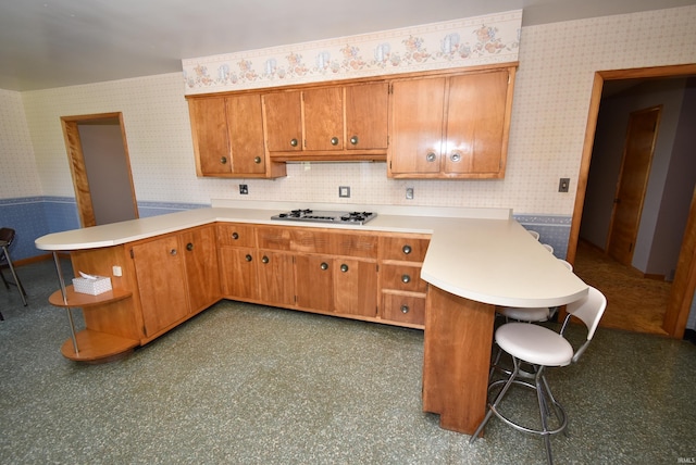 kitchen with a kitchen bar, kitchen peninsula, decorative backsplash, and stainless steel gas cooktop