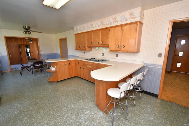 kitchen with tasteful backsplash, a kitchen breakfast bar, stainless steel gas stovetop, kitchen peninsula, and ceiling fan