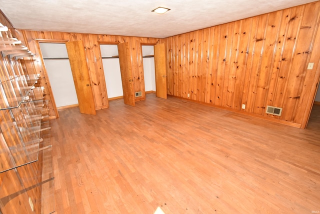 interior space featuring wood walls, a textured ceiling, and light hardwood / wood-style flooring