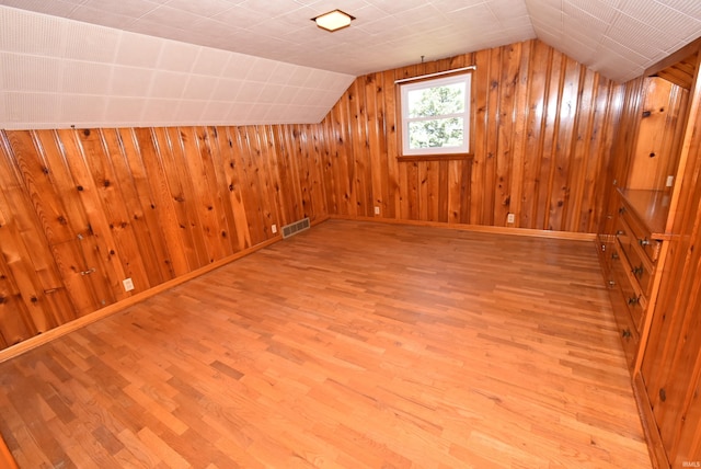 bonus room featuring lofted ceiling, wooden walls, and light hardwood / wood-style floors