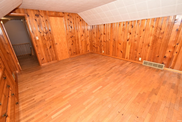 spare room featuring light wood-type flooring, wooden walls, radiator, and vaulted ceiling