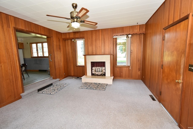 living room with plenty of natural light, light colored carpet, wooden walls, and a fireplace