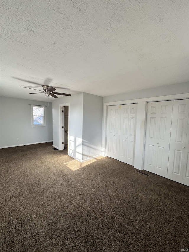 unfurnished bedroom featuring carpet floors, ceiling fan, a textured ceiling, and multiple closets