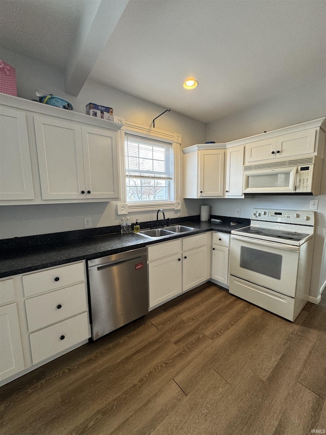 kitchen with white appliances, dark countertops, dark wood-type flooring, white cabinetry, and a sink