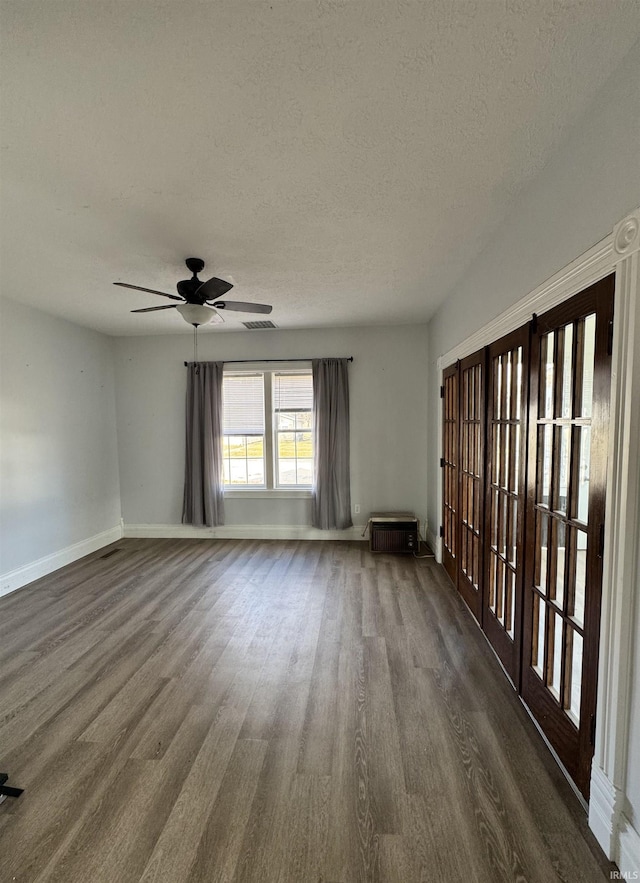 empty room with visible vents, baseboards, a ceiling fan, dark wood-type flooring, and a textured ceiling