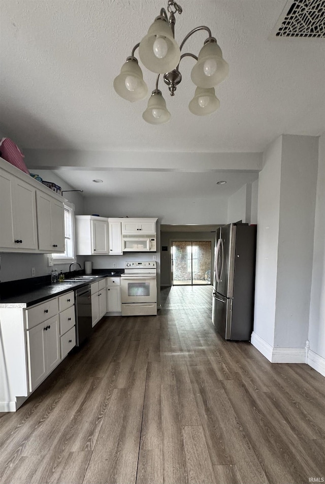 kitchen featuring white appliances, a sink, visible vents, dark wood-style floors, and dark countertops