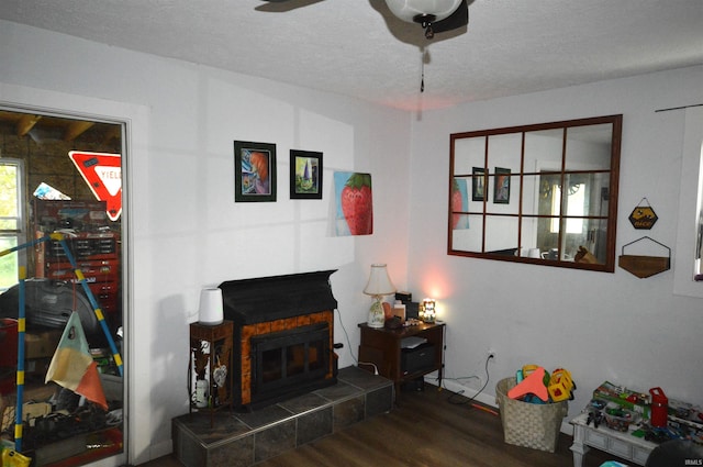 living room with ceiling fan, dark hardwood / wood-style floors, a textured ceiling, and a tile fireplace