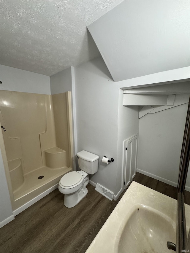 bathroom with a textured ceiling, toilet, wood finished floors, visible vents, and a stall shower