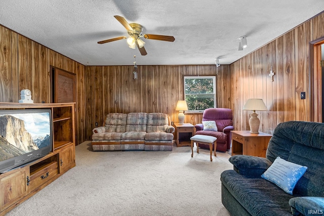 carpeted living room with wood walls, ceiling fan, and a textured ceiling