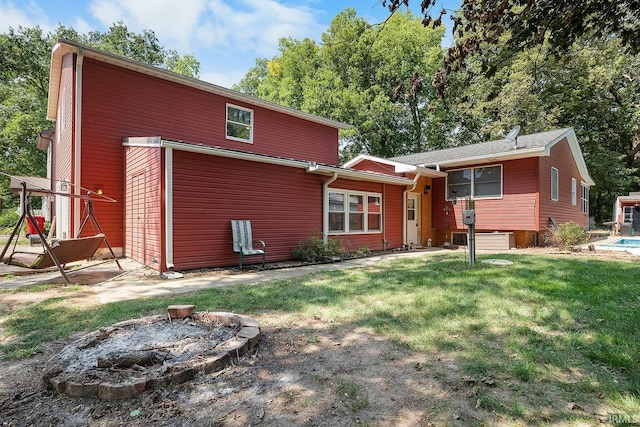 back of house with a lawn and an outdoor fire pit