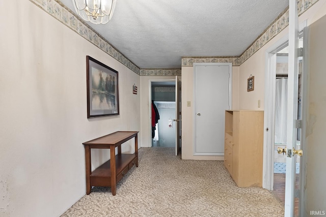 corridor with light colored carpet, a chandelier, and a textured ceiling