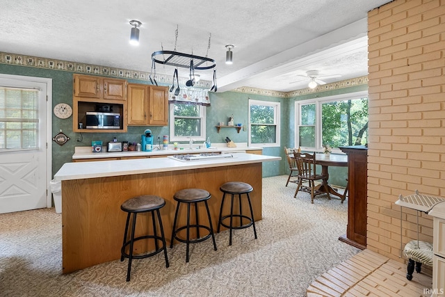 kitchen with ceiling fan, a kitchen bar, light carpet, and a textured ceiling