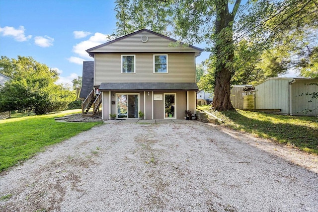 view of front of home with an outbuilding, a storage unit, stairs, driveway, and a front lawn