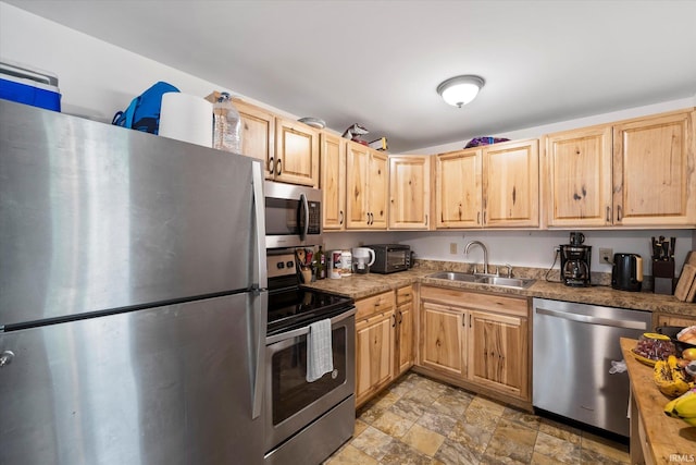 kitchen featuring stainless steel appliances, stone finish flooring, light brown cabinets, and a sink