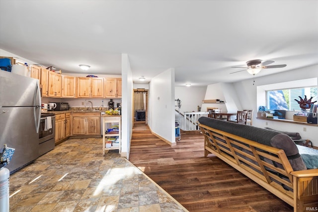 kitchen with stainless steel appliances, a sink, open floor plan, wall chimney range hood, and light brown cabinetry