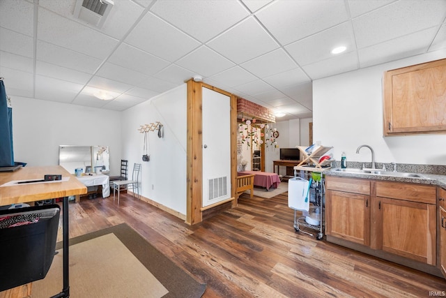 kitchen featuring dark wood-type flooring, a paneled ceiling, a sink, and visible vents