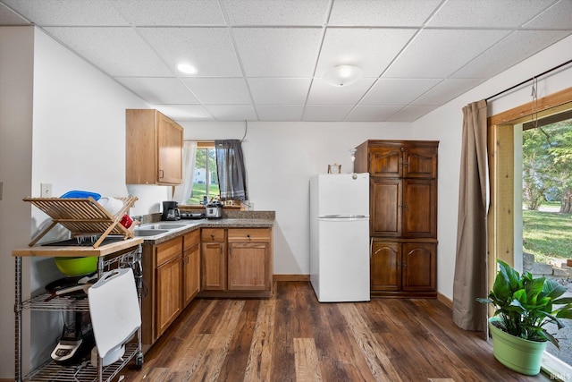 kitchen with dark wood finished floors, freestanding refrigerator, a sink, a drop ceiling, and baseboards