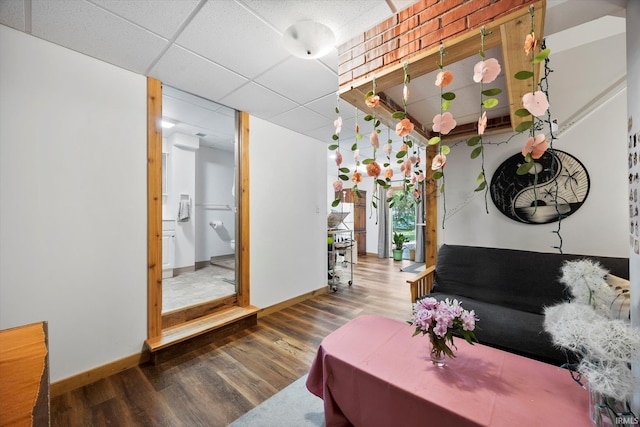 living room featuring baseboards, a drop ceiling, and wood finished floors