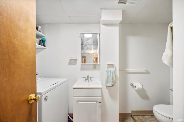 bathroom featuring a drop ceiling, toilet, visible vents, vanity, and washer / dryer