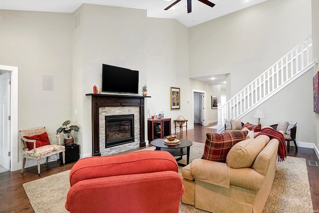 living room featuring dark wood-type flooring, high vaulted ceiling, ceiling fan, and a stone fireplace