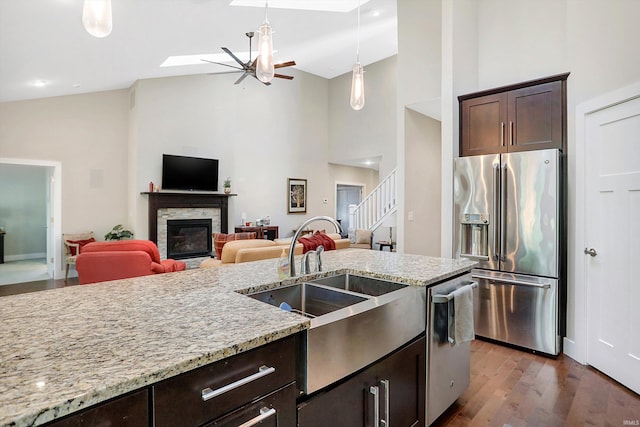 kitchen with a fireplace, high vaulted ceiling, stainless steel appliances, dark hardwood / wood-style flooring, and sink