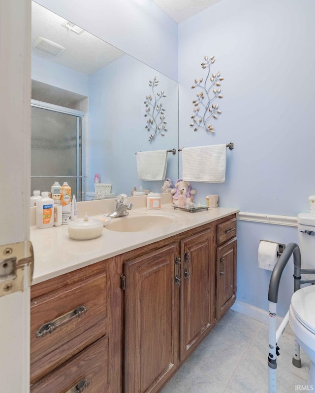 bathroom with toilet, tile patterned floors, a shower with door, vanity, and a textured ceiling