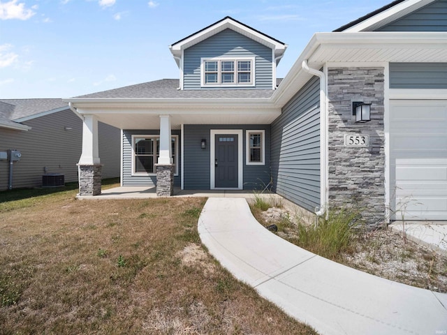 entrance to property with a garage, a porch, a yard, and cooling unit