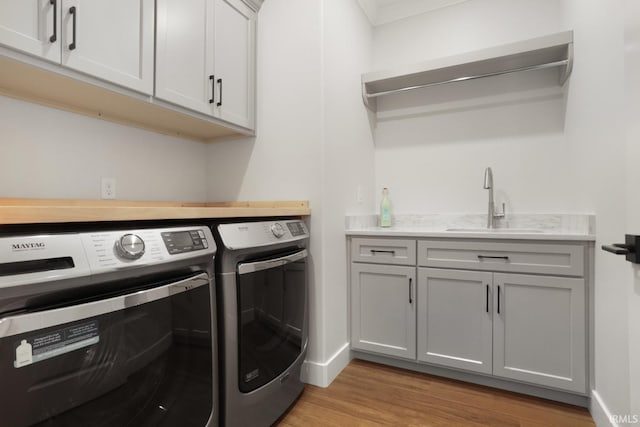 laundry area featuring cabinets, washing machine and dryer, sink, and light hardwood / wood-style floors