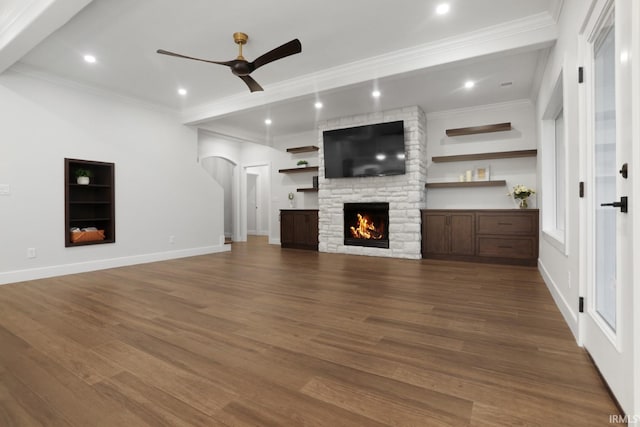 unfurnished living room with ornamental molding, hardwood / wood-style flooring, ceiling fan, and a stone fireplace