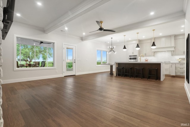 unfurnished living room featuring crown molding, dark hardwood / wood-style flooring, beam ceiling, and ceiling fan