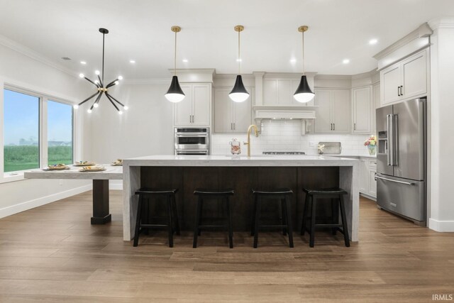 kitchen with backsplash, crown molding, appliances with stainless steel finishes, wood-type flooring, and a kitchen island with sink