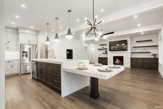 kitchen with white cabinetry, decorative backsplash, a stone fireplace, appliances with stainless steel finishes, and hardwood / wood-style flooring