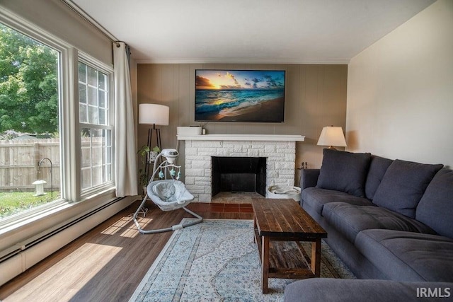 living room with a healthy amount of sunlight, baseboard heating, wood finished floors, and a stone fireplace