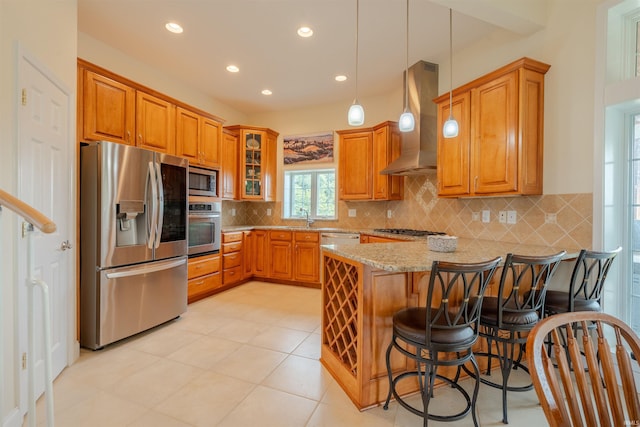kitchen with stainless steel appliances, exhaust hood, light stone counters, a peninsula, and brown cabinets