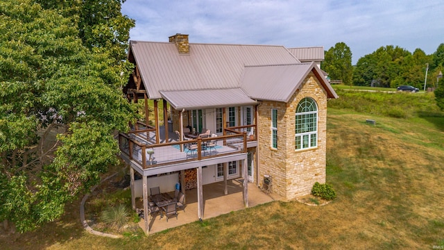 rear view of property featuring stone siding, a chimney, a lawn, and a patio