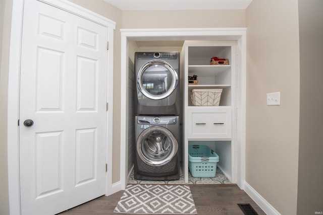 clothes washing area featuring stacked washer and dryer, laundry area, dark wood-style flooring, visible vents, and baseboards