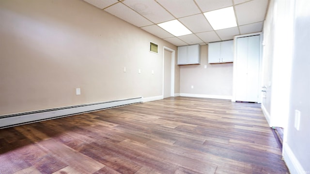 empty room with a paneled ceiling, wood-type flooring, and a baseboard radiator