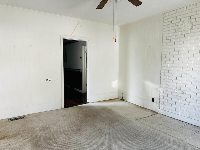 carpeted spare room featuring visible vents, brick wall, a ceiling fan, and ornamental molding