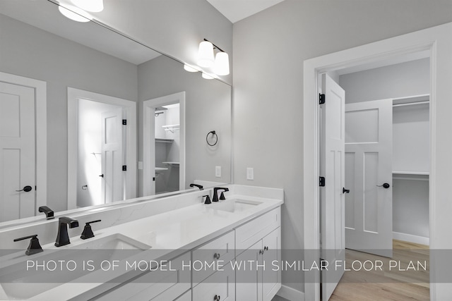 full bath with double vanity, a spacious closet, a sink, and wood finished floors