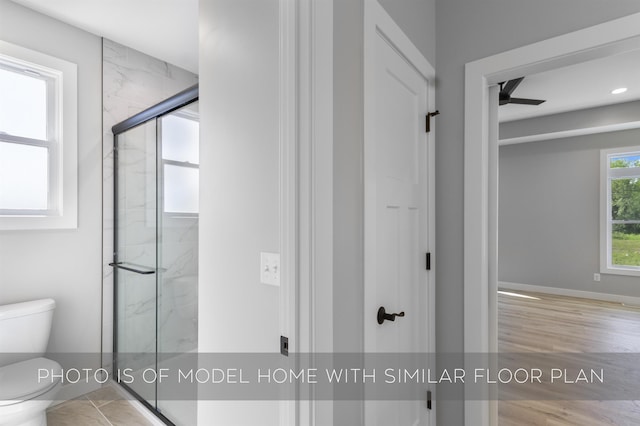 bathroom featuring ceiling fan, toilet, wood finished floors, baseboards, and a marble finish shower