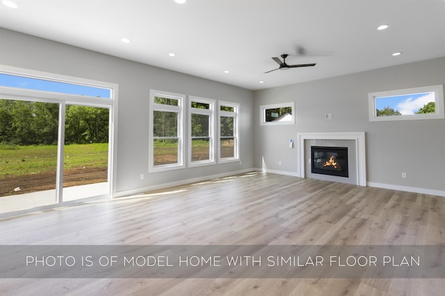 unfurnished living room featuring wood finished floors, a glass covered fireplace, a wealth of natural light, and recessed lighting