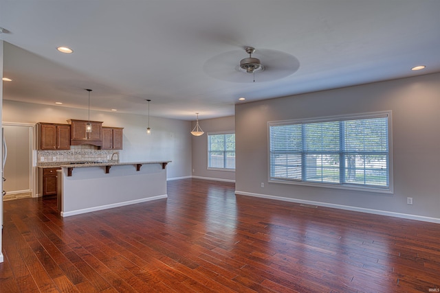 kitchen featuring dark wood-type flooring, a wealth of natural light, ceiling fan, and a breakfast bar